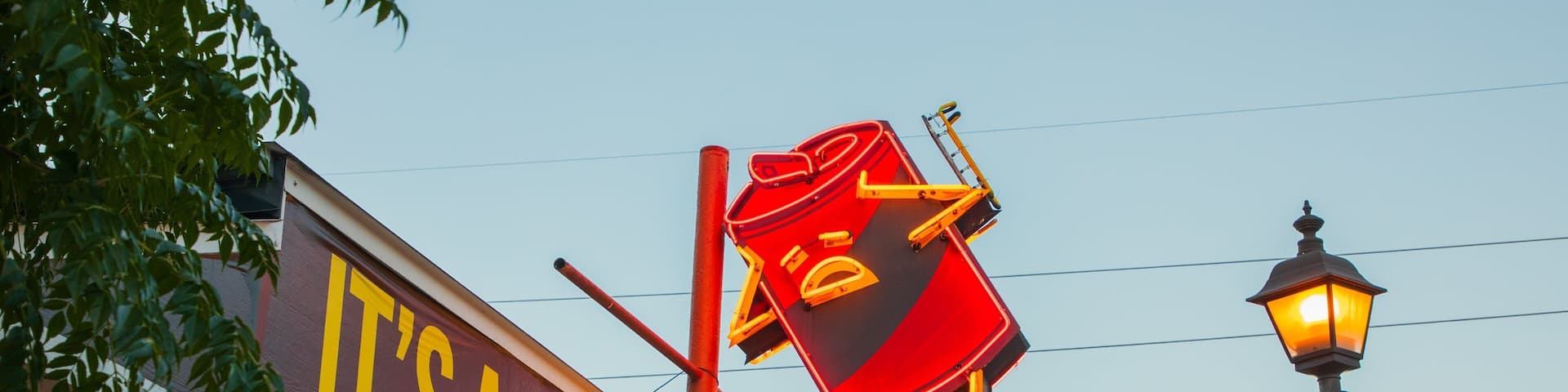 A bar named "It's a Bar" with a neon sign for "Latchkey Patio" and a street lamp.