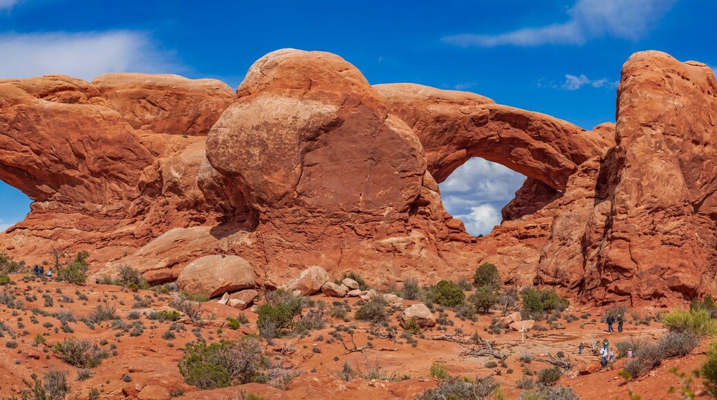 Panoramic view of North Window, South Window, and Turret Arch with beautiful clouds in the sky, small figures of people in the frame emphasize the scale and beauty of this majestic creation, Moab, USA