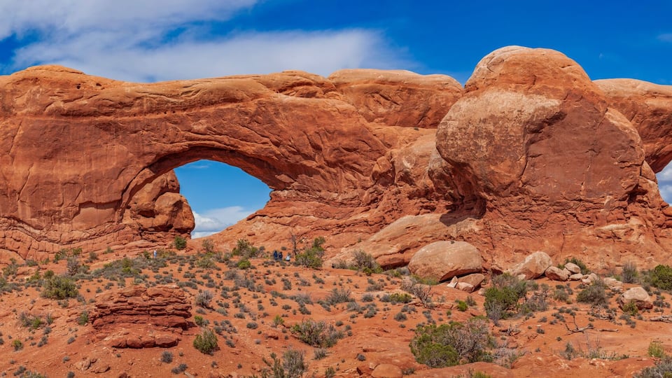 Panoramic view of North Window, South Window, and Turret Arch with beautiful clouds in the sky, small figures of people in the frame emphasize the scale and beauty of this majestic creation, Moab, USA