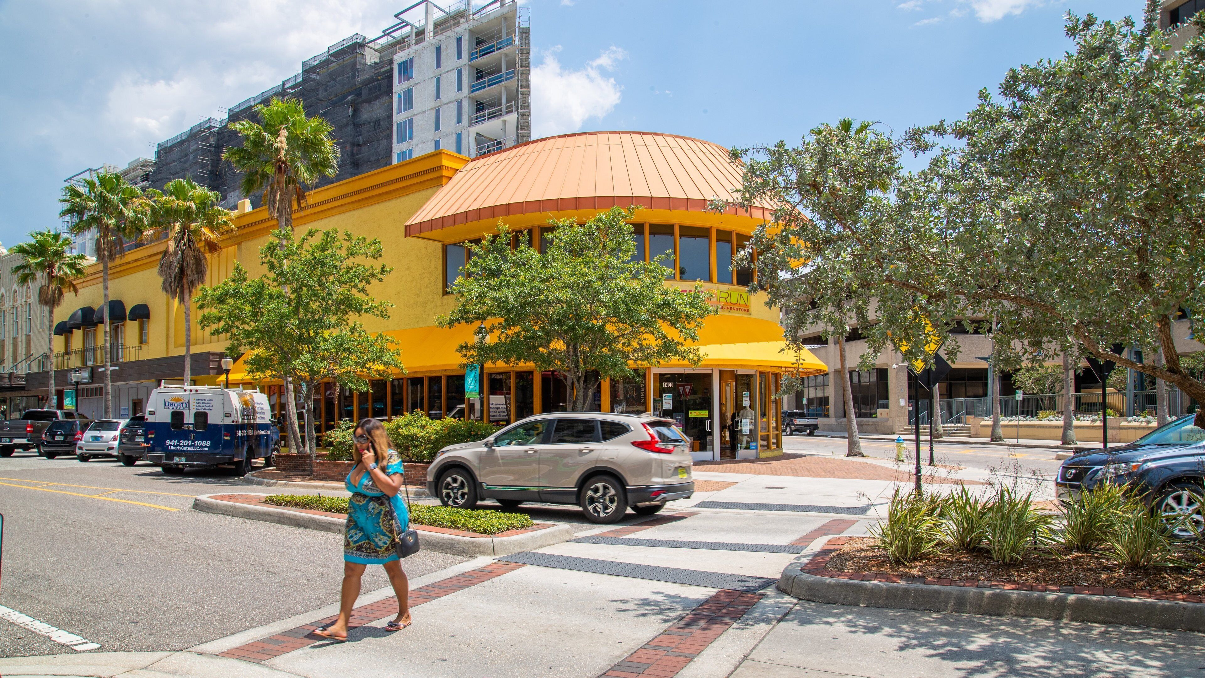 A yellow building with a red roof, palm trees, and a street with cars.