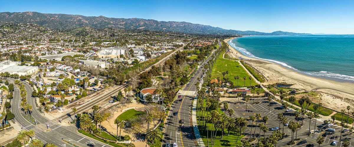 A coastal city with a beach, roads, and mountains in the background.