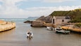 A harbor with boats, a stone building, and a rocky coastline.
