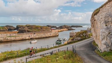A coastal road with a cyclist, a boat, and rocky cliffs.