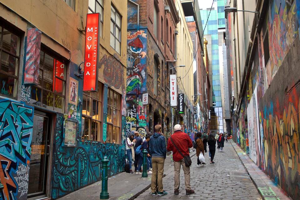 En smal gränd med färgglad graffiti och väggmålningar, folk som promenerar och olika butiksskyltar.