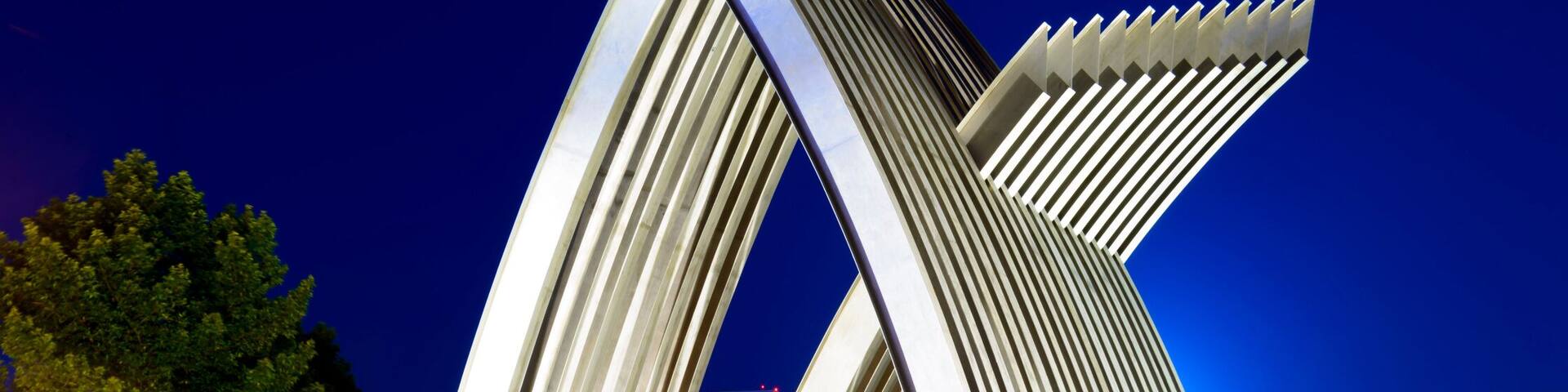A modern architectural structure with curved, ribbed design elements, set against a night sky.