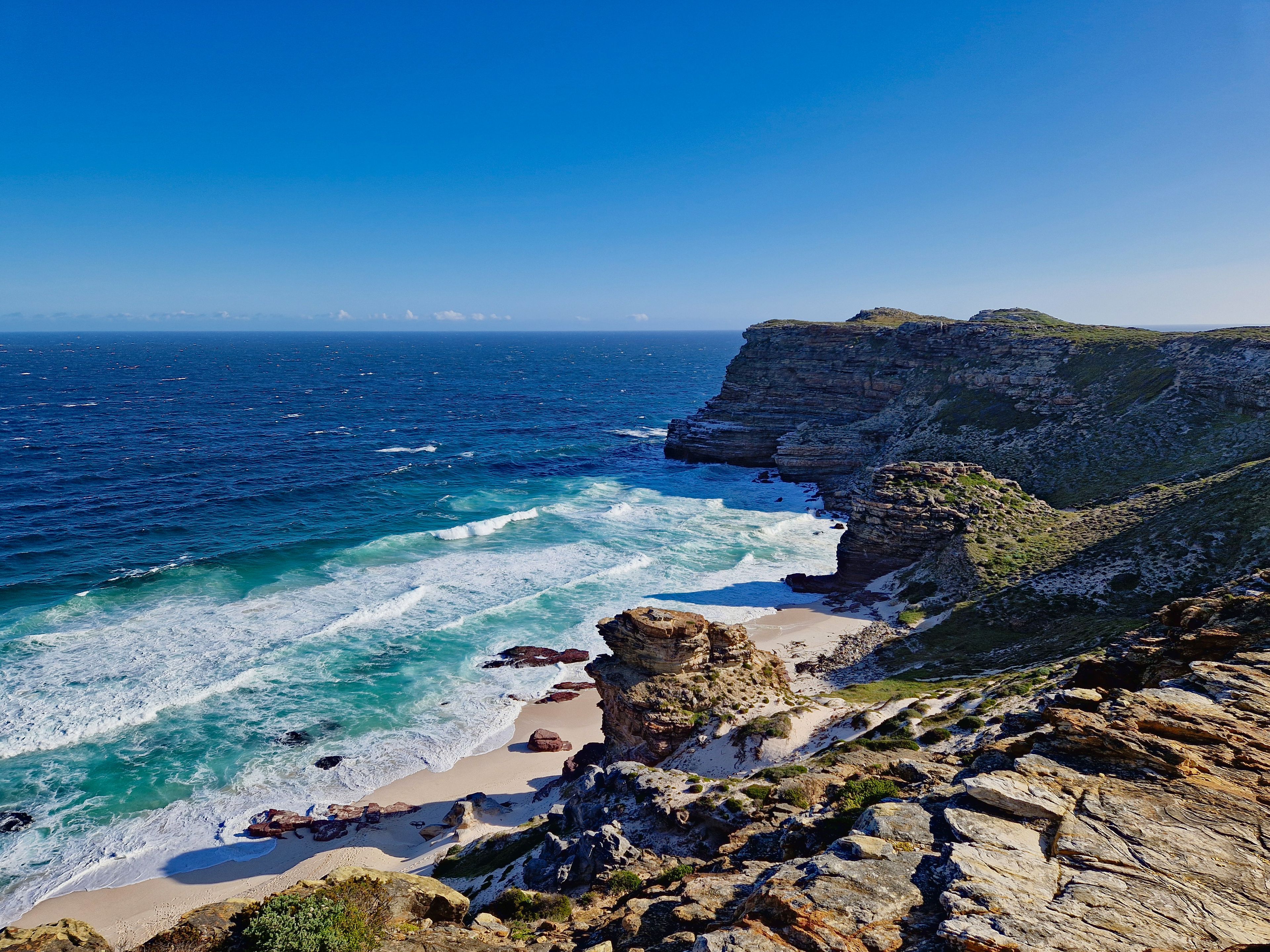 A coastal landscape with a rocky beach, clear blue ocean, and a cliff.