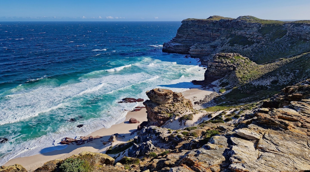 A coastal landscape with a rocky beach, clear blue ocean, and a cliff.