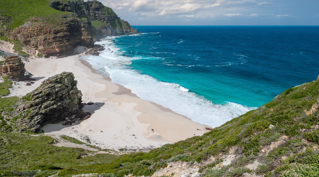 A coastal landscape with a sandy beach, rocky cliffs, and a lighthouse on a hill.