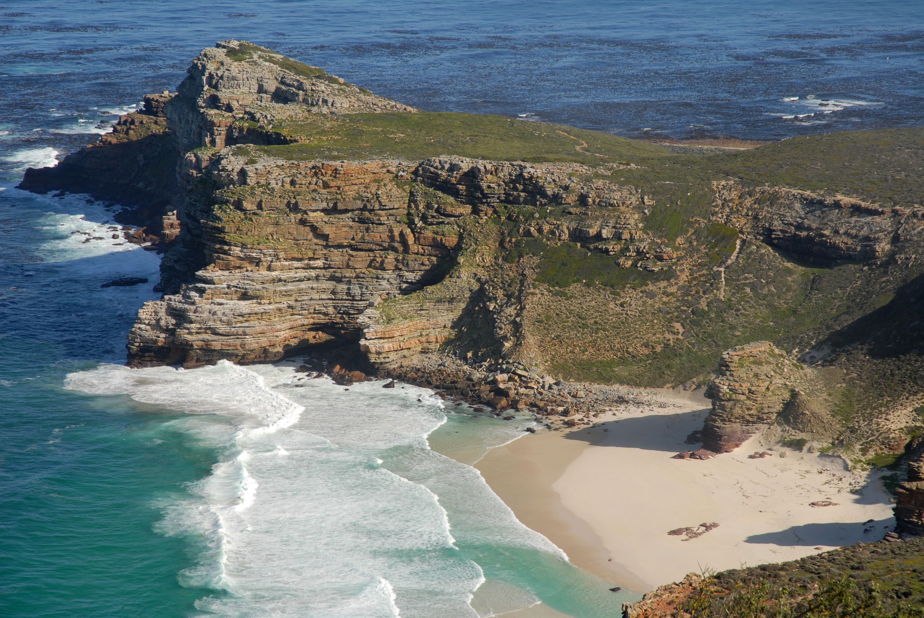 A coastal landscape with a prominent rocky cliff, a sandy beach, and the ocean.
