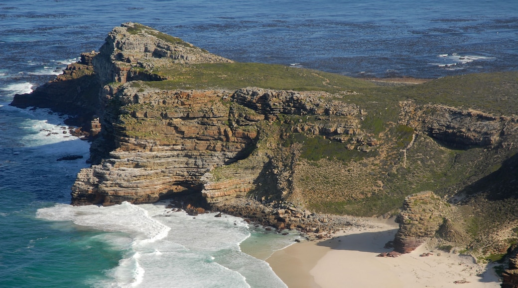 A coastal landscape with a prominent rocky cliff, a sandy beach, and the ocean.