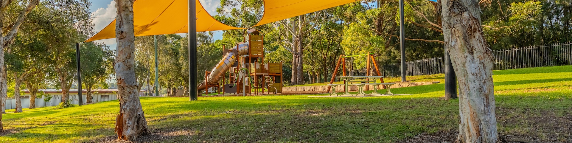 Ein Spielplatz mit Rutsche und Klettergerüsten, umgeben von Bäumen und einer Rasenfläche.