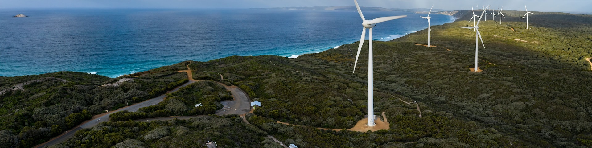 A coastal landscape with wind turbines and a road leading to a small building.