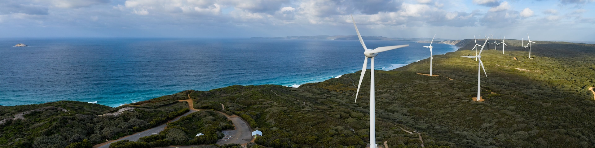 A coastal landscape with wind turbines and a road leading to a small building.
