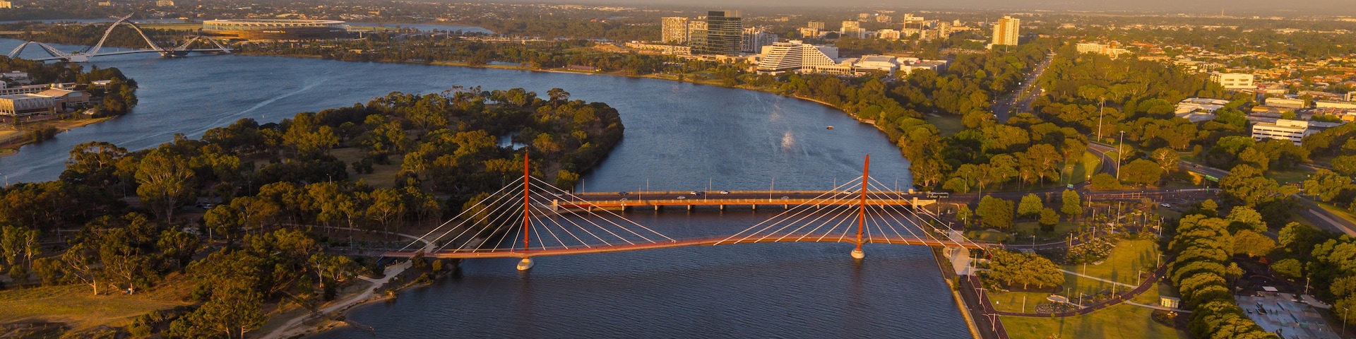 Uma grande ponte suspensa sobre um rio, cercada por vegetação e edifícios urbanos.