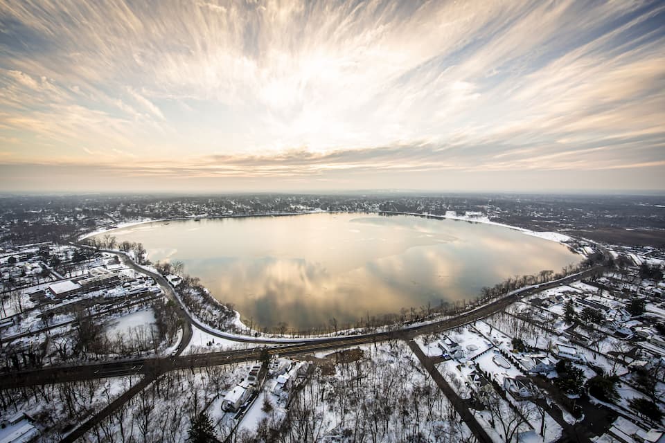 Vista aérea de un lago extenso rodeado de edificios y caminos cubiertos de nieve.