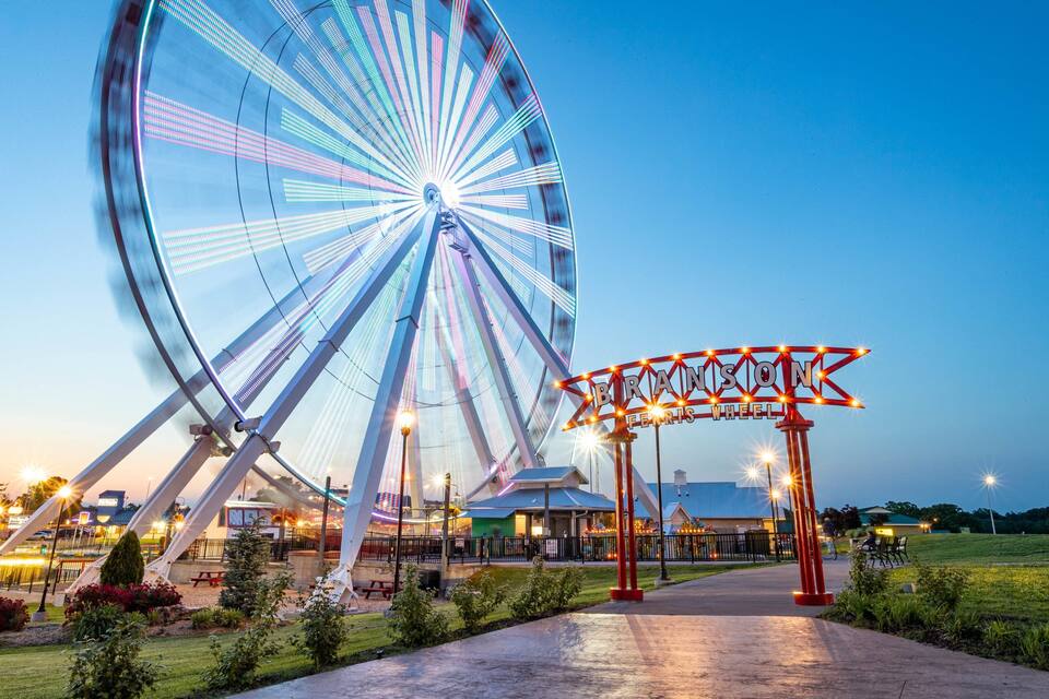 A large Ferris wheel with a sign that reads "BRANSON FERRIS WHEEL" in a park at dusk.