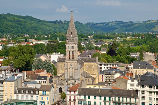 A town with a prominent church featuring a tall spire, surrounded by residential buildings and lush green hills in the background.