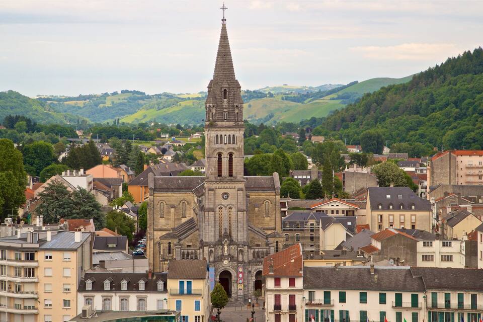A historic church with a tall spire, surrounded by a town with buildings and hills in the background.