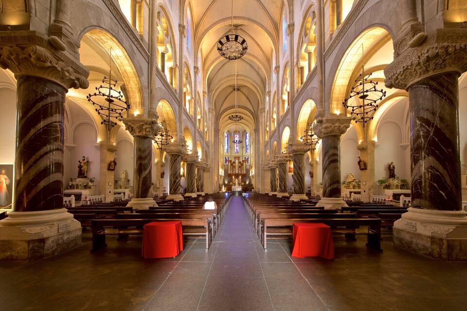 Interior imponente de una catedral, con altos techos abovedados, columnas de mármol e hileras de bancas.
