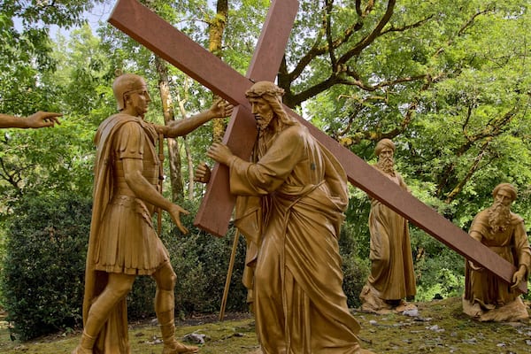 A bronze statue of Jesus carrying a cross, surrounded by other figures in a forested area.