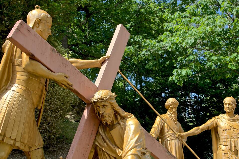 A golden statue of a man carrying a cross, surrounded by trees.