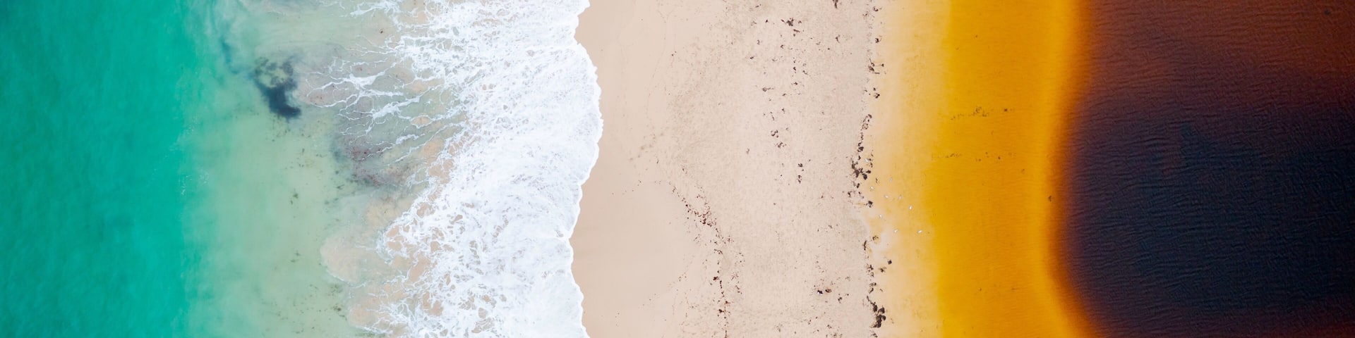 A beach with turquoise water, white waves, and a sandy shore.
