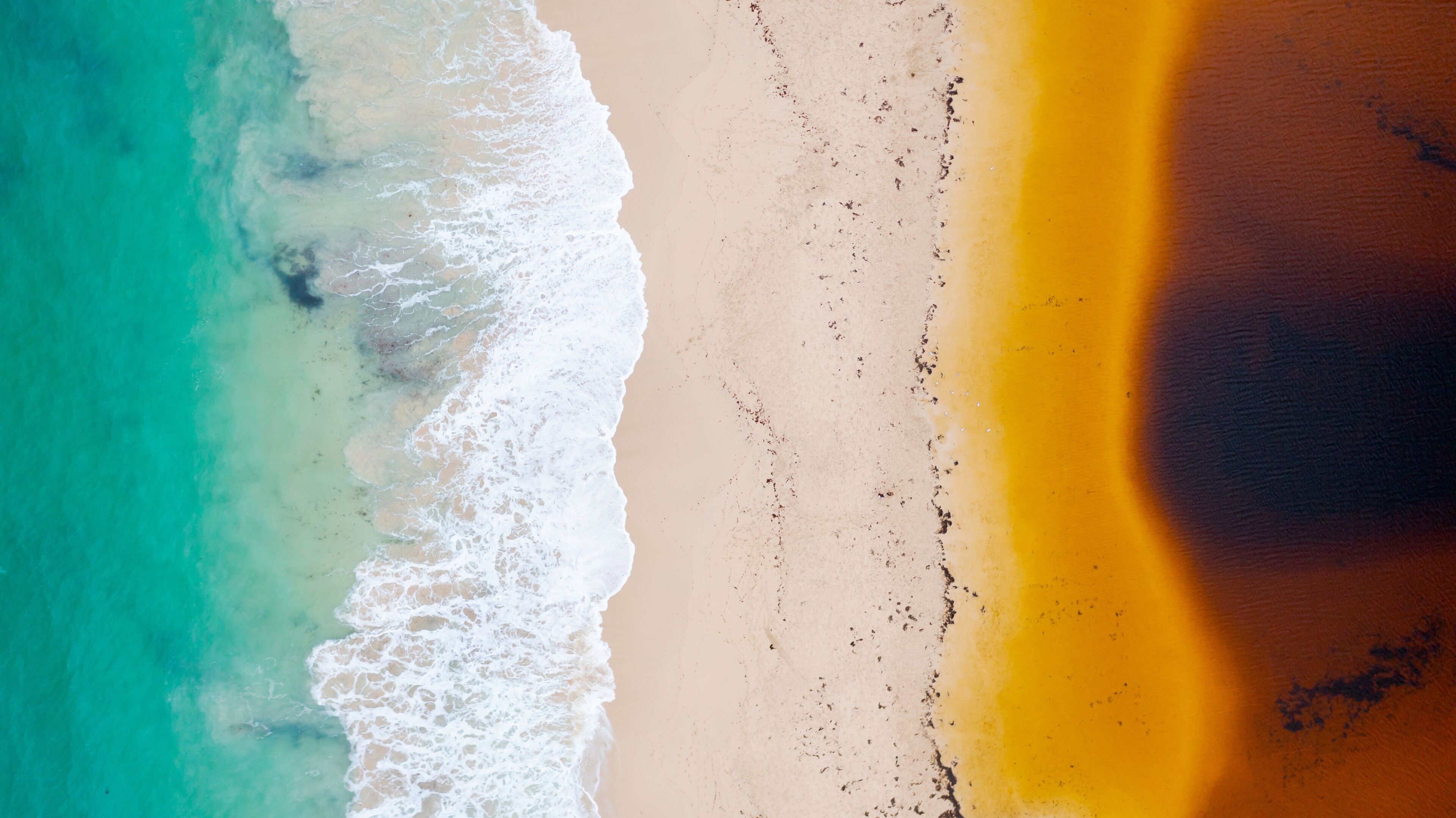 A beach with turquoise water, white waves, and a sandy shore.