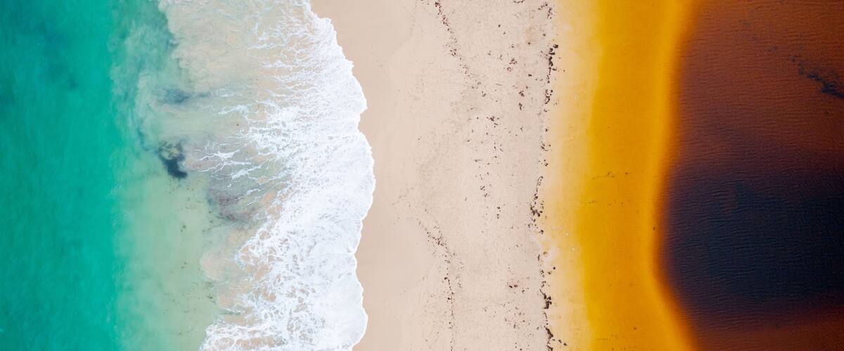 A beach with turquoise water, white waves, and a sandy shore.