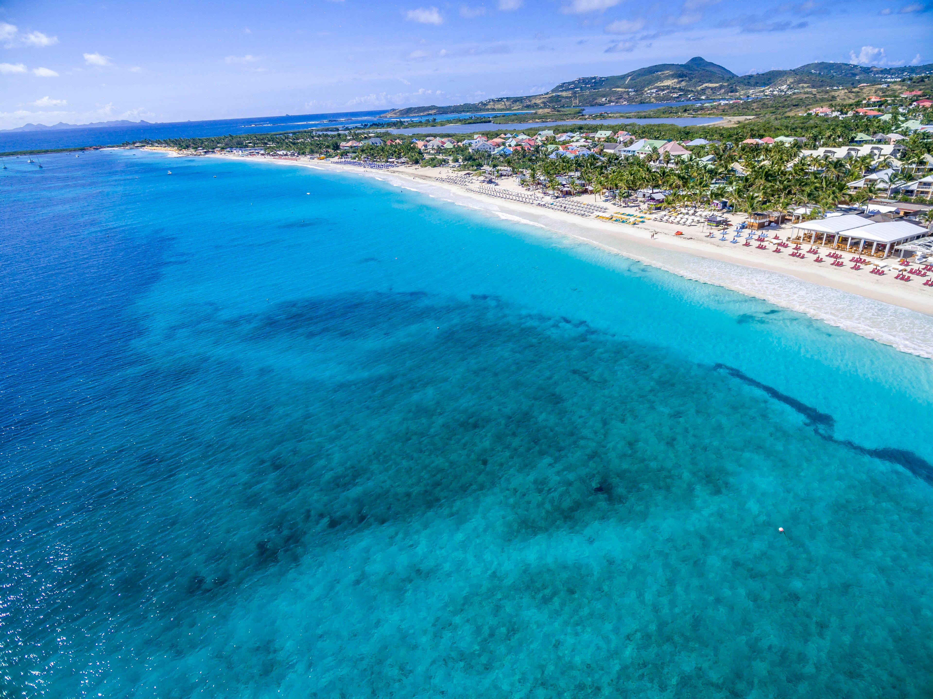 A coastal town with a clear blue sea, sandy beaches, and a backdrop of mountains.