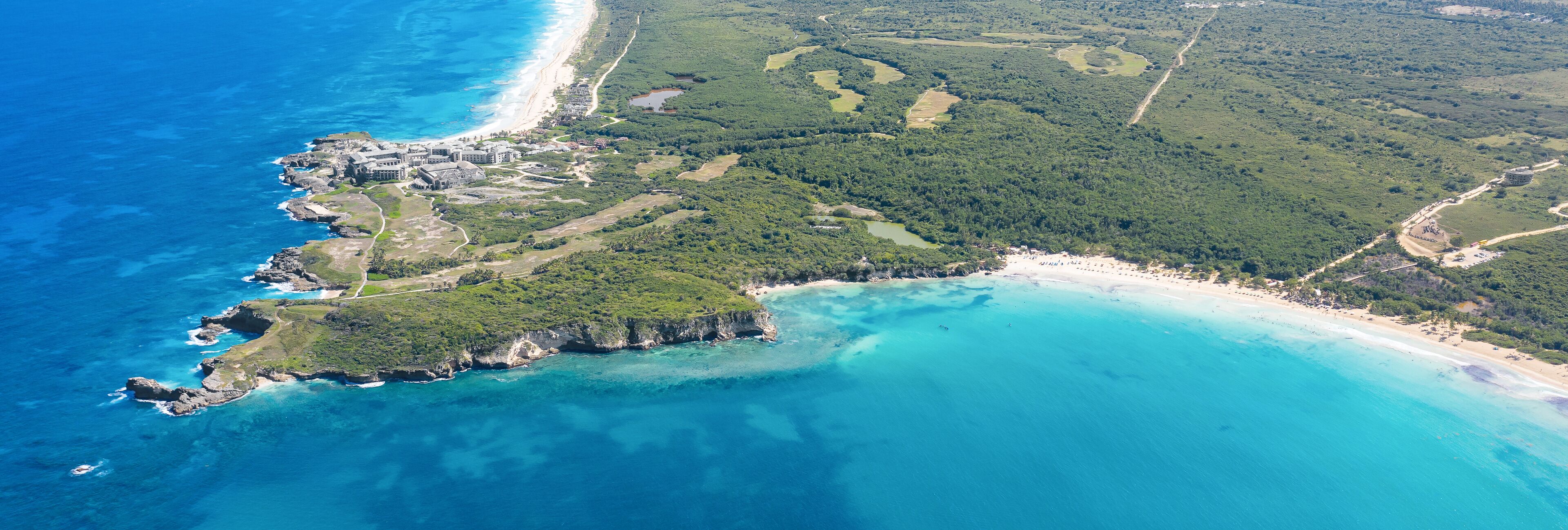 An aerial view of a coastal area with a beach, cliffs, and a dense forest.