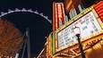 Ein hell beleuchtetes Marquee mit Neonlichtern, im Hintergrund ein Riesenrad, und ein Marquee mit Auflistung von Live-Musik und Bowling-Veranstaltungen.