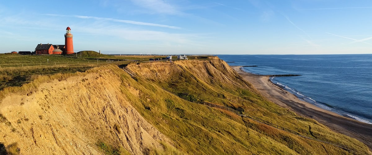 A coastal landscape with a lighthouse, grassy cliffs, and a beach.