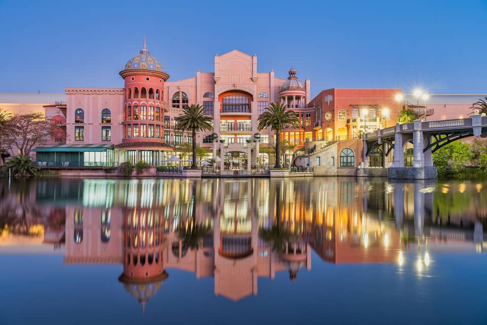 A waterfront with a reflection of buildings, palm trees, and a bridge.