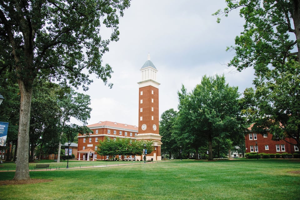 A large brick building with a clock tower, surrounded by green grass and trees.