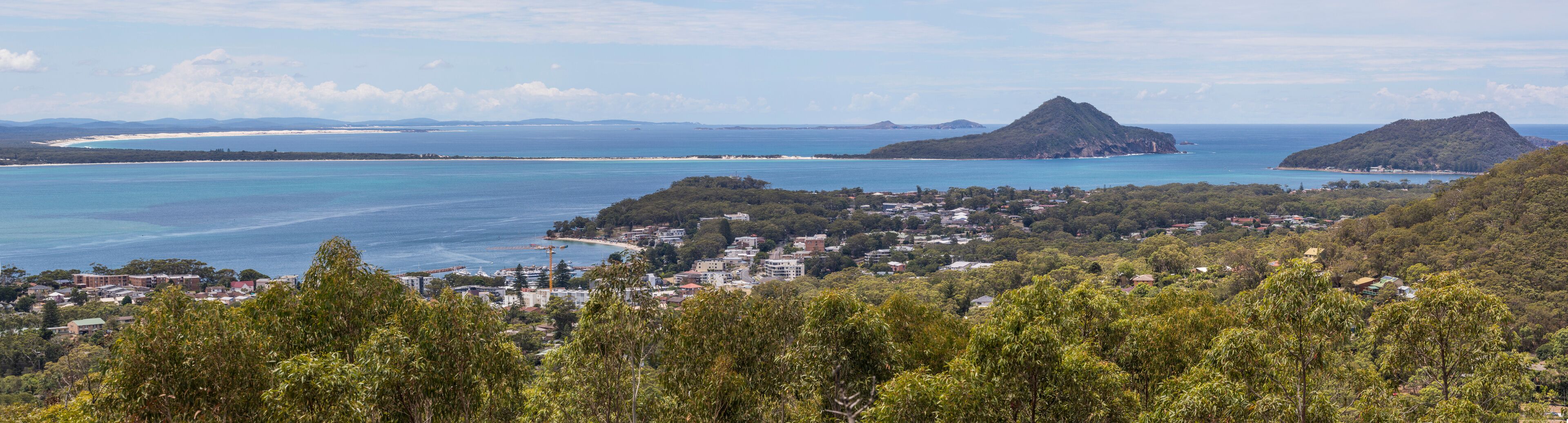 A coastal town with a beach, forested hills, and a mountain in the distance.