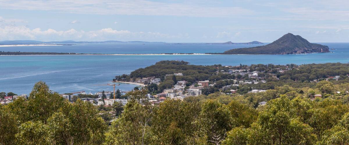A coastal town with a beach, forested hills, and a mountain in the distance.