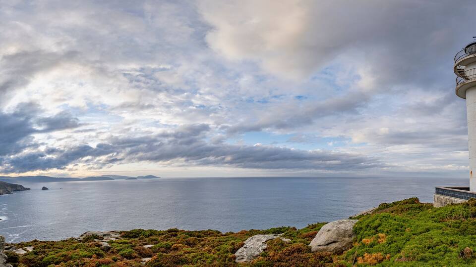 A lighthouse on a rocky coastline with a cloudy sky.