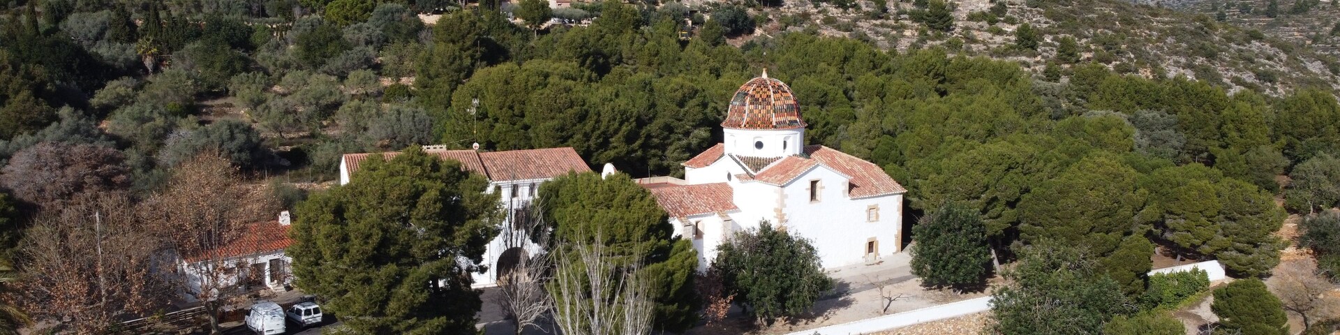 A white church with a dome on a hill surrounded by trees and a mountain in the background.