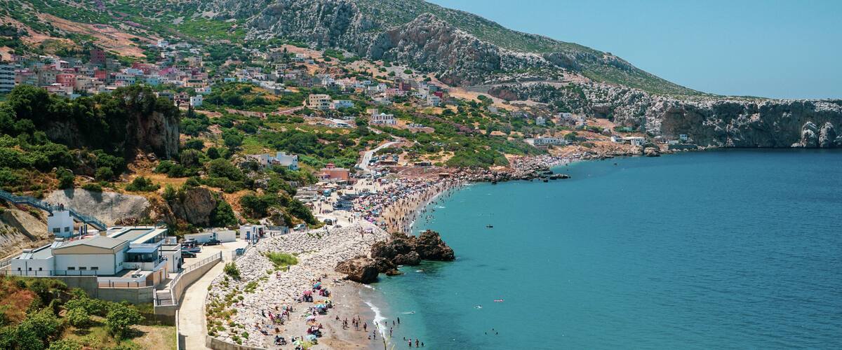 A coastal town with a beach, rocky cliffs, and a mountainous backdrop.