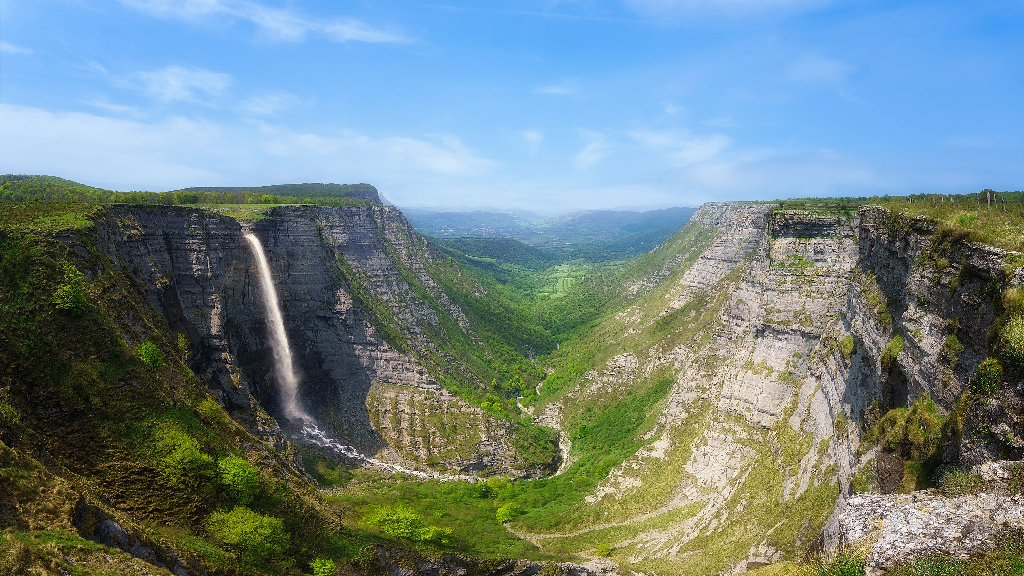 Un cañón con una cascada, vegetación exuberante y un río.