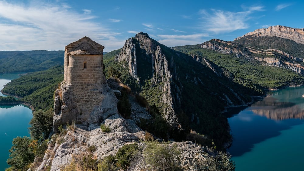 Ein Turm auf einer Klippe mit Blick auf einen See, der von Bergen umgeben ist.