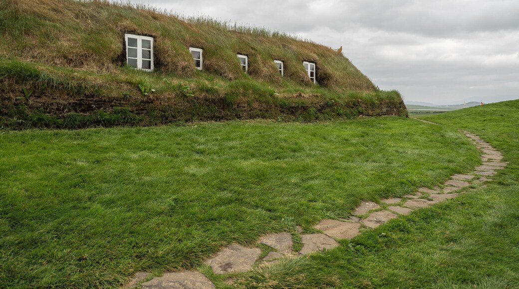 Un paisaje con césped, un sendero de piedra que conduce a una colina cubierta de hierba con cuatro ventanas.