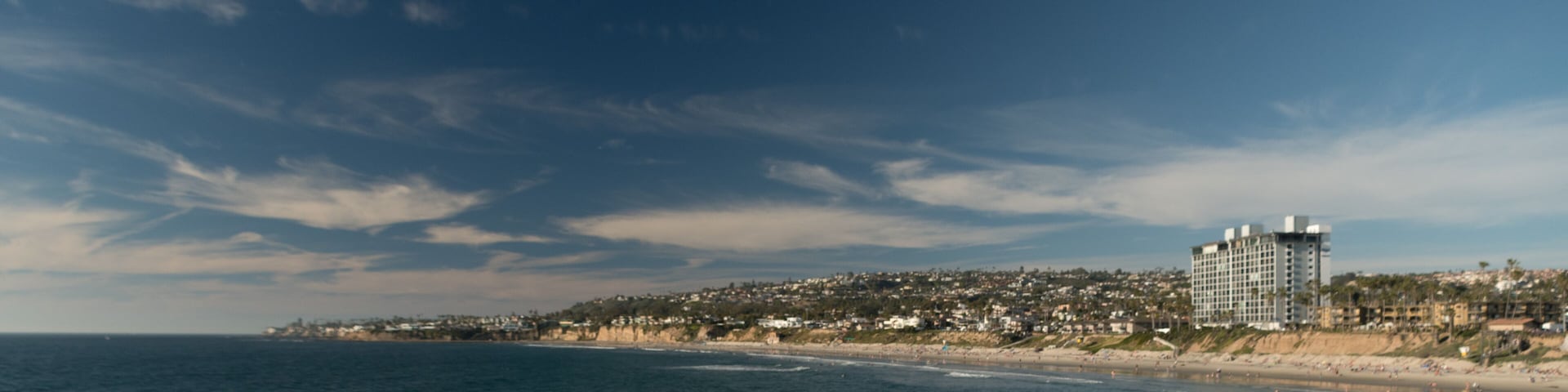 A coastal cityscape with a beach, ocean, and a dense residential area with a prominent hotel.