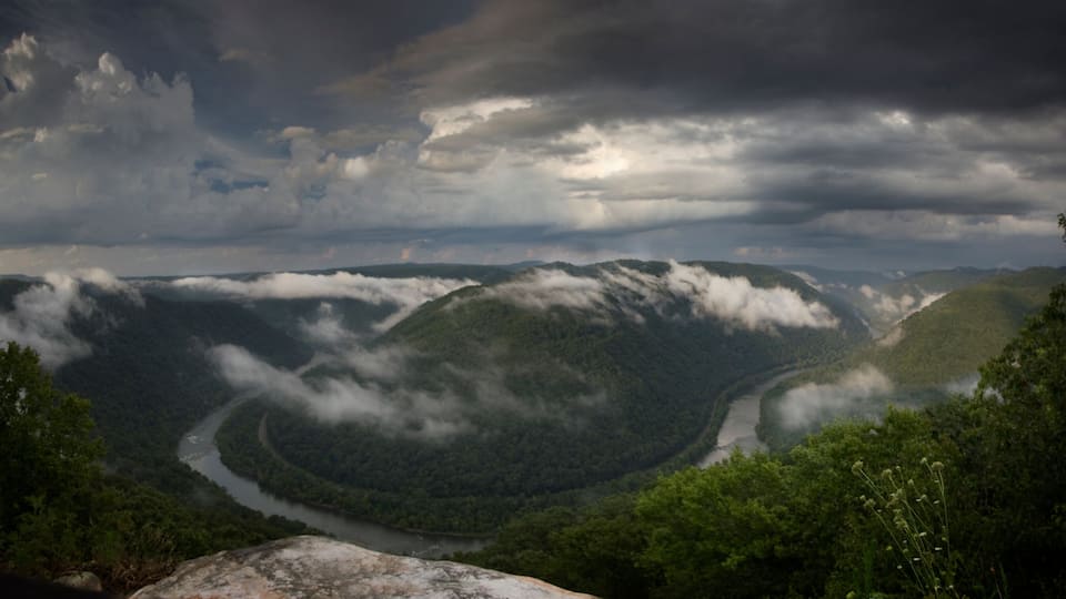 A river winding through a valley with dense forest and misty clouds above.