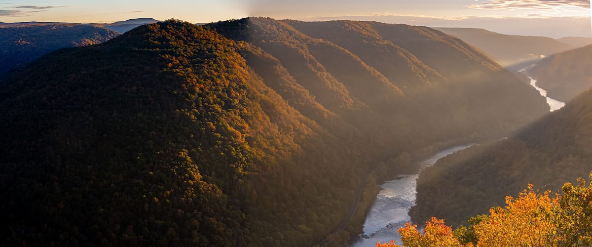 Un río serpentea por un paisaje montañoso con densos bosques y follaje otoñal.