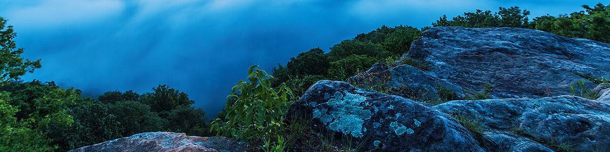 A mountain landscape with a view of the sky at sunset, featuring clouds below the mountain peak.