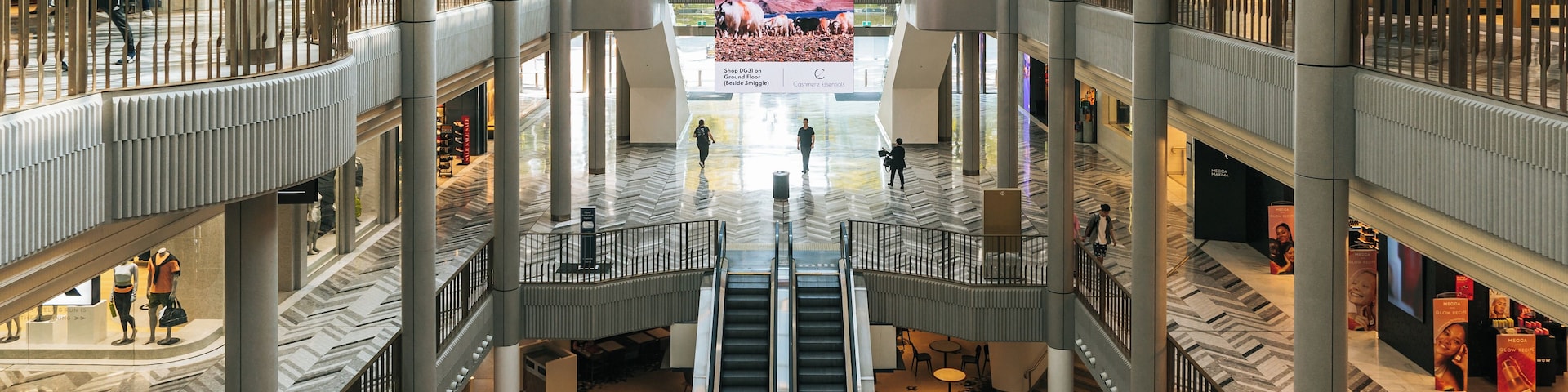 A multi-level shopping mall with escalators, glass railings, and various stores.