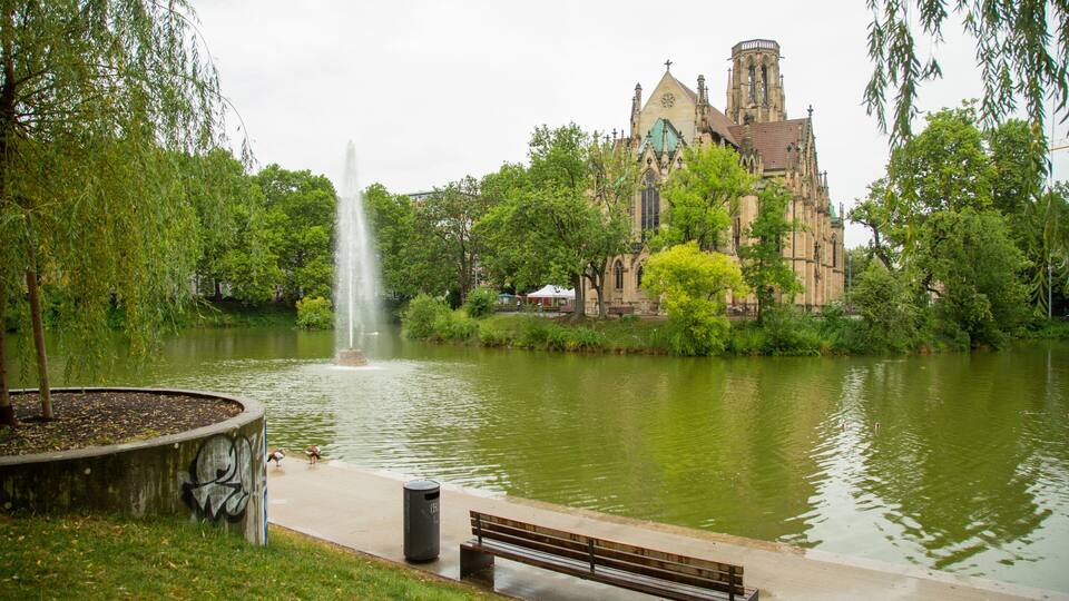 A park with a fountain, a bench, and a historic church.