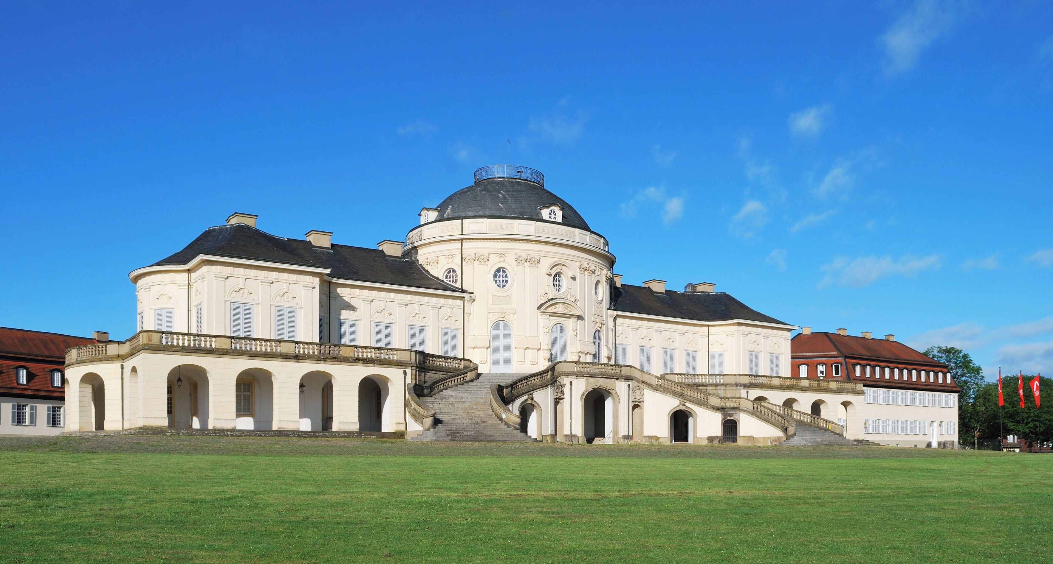 A large, historic building with a central dome, arched windows, and a grand staircase leading to the entrance.