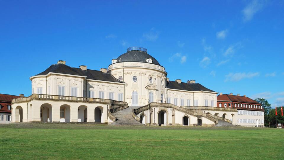 A large, historic building with a central dome, arched windows, and a grand staircase leading to the entrance.